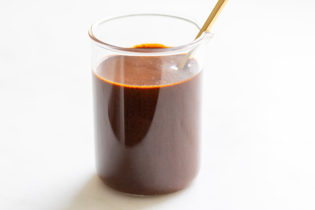 A small clear glass jar filled with enchilada sauce on a white countertop.