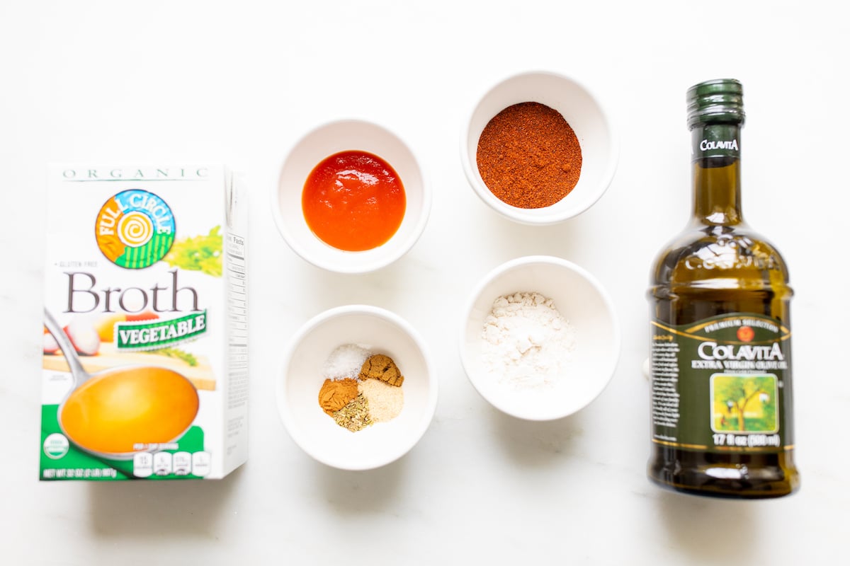 Ingredients for a homemade enchilada sauce recipe laid out on a marble countertop.