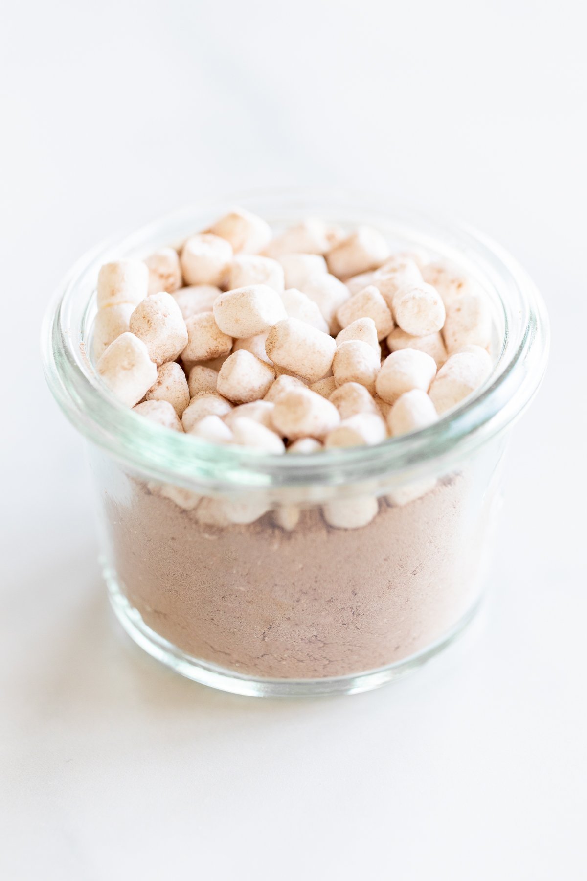 Homemade hot chocolate with marshmallows in a glass bowl on a white surface.