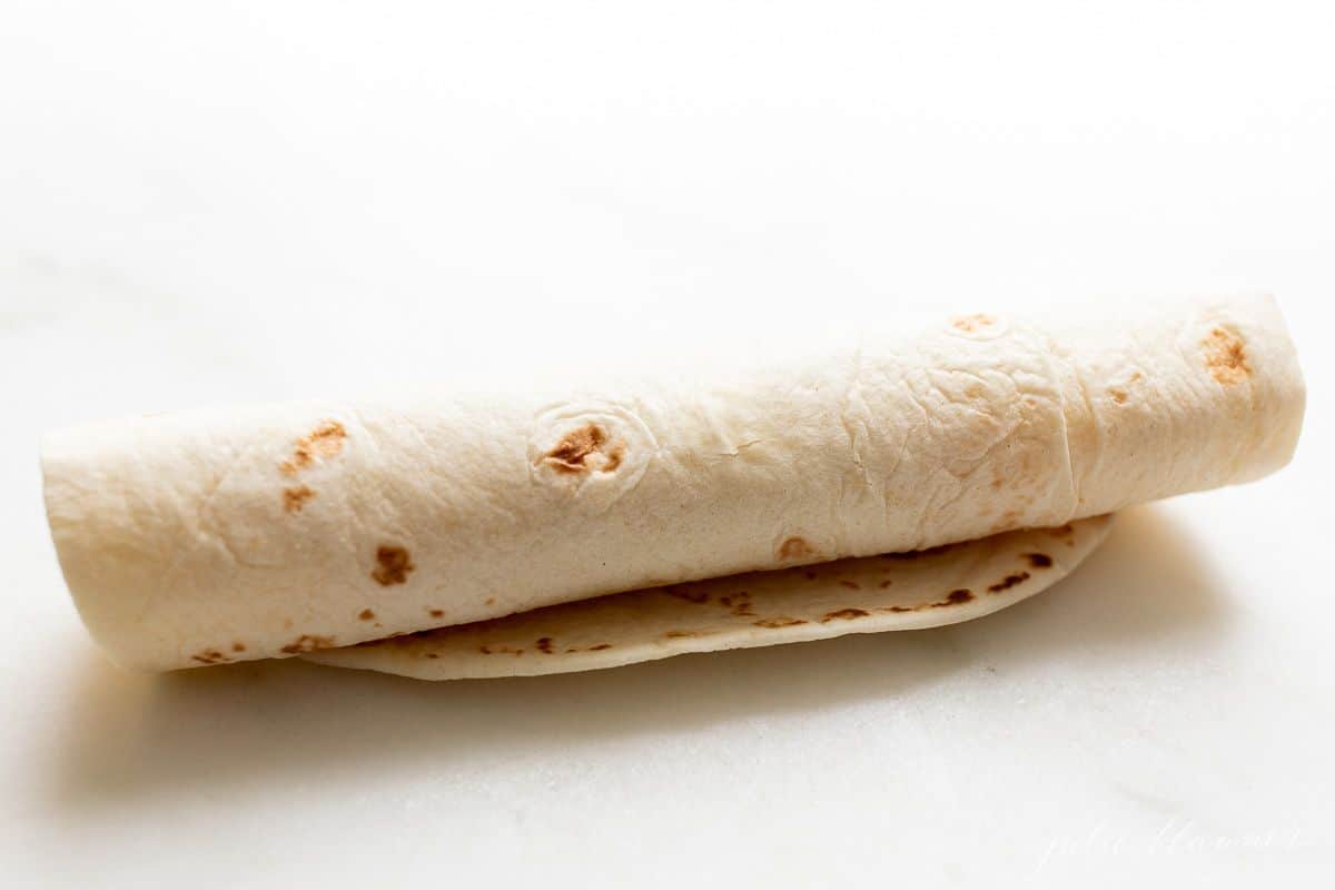 A flour tortilla rolled up on a marble surface.