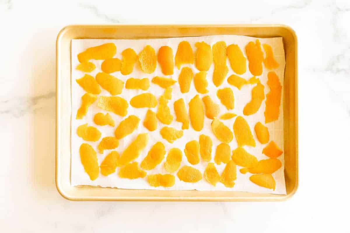 A gold sheet pan lined with parchment paper and covered in dried orange peels.