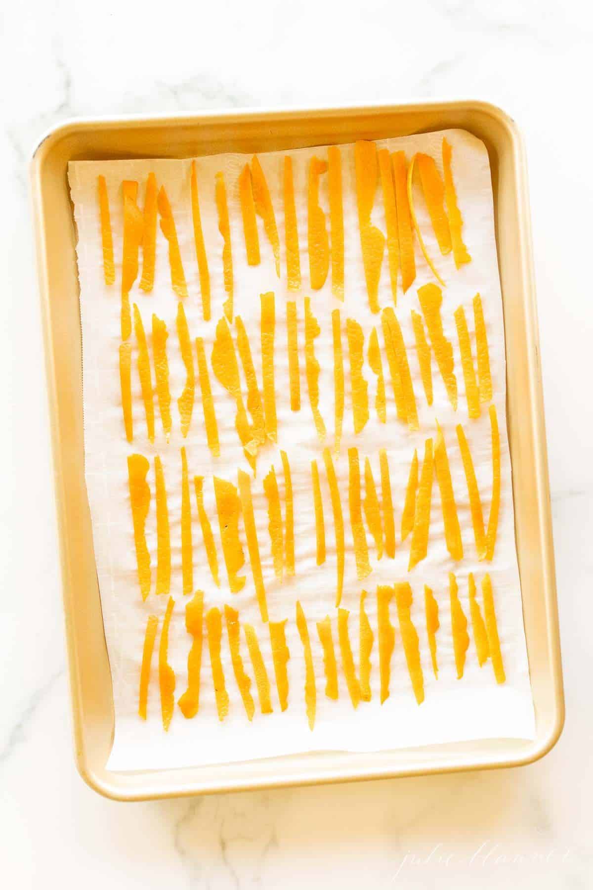 A gold sheet pan lined with parchment paper and covered in dried orange peel slices.