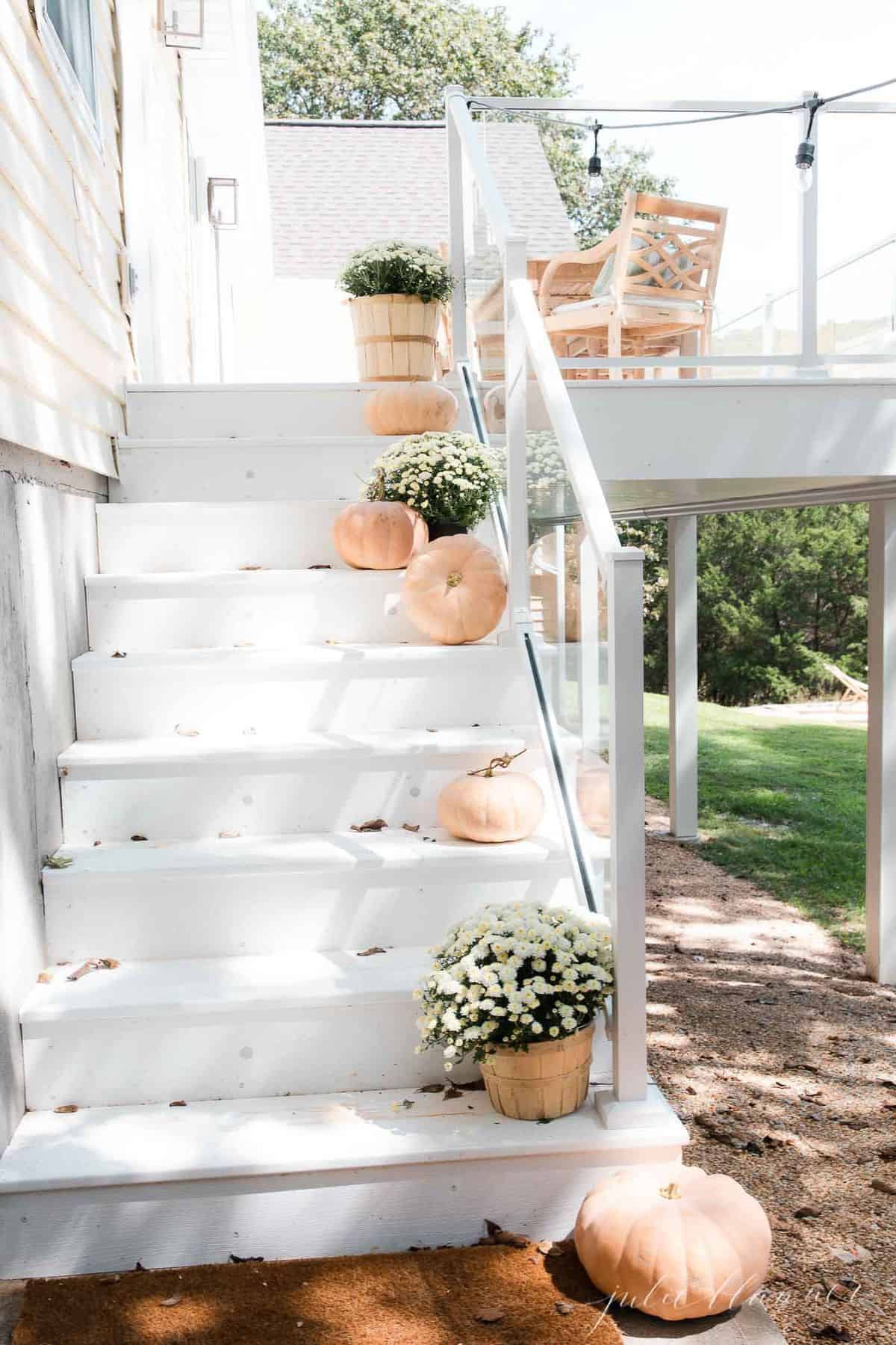 White deck steps decorated with minimalist fall decor, peach pumpkins and white mums.