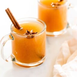 A pair of glass mugs full of pear cider, cinnamon sticks for garnish.