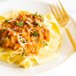 A white plate with a serving of braised pork ragu with pappardelle