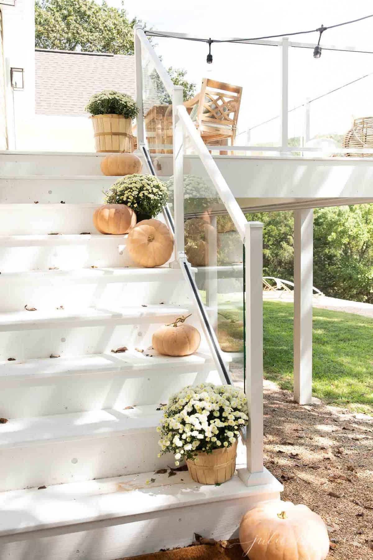 White deck steps decorated with minimalist fall decor, peach pumpkins and white mums.