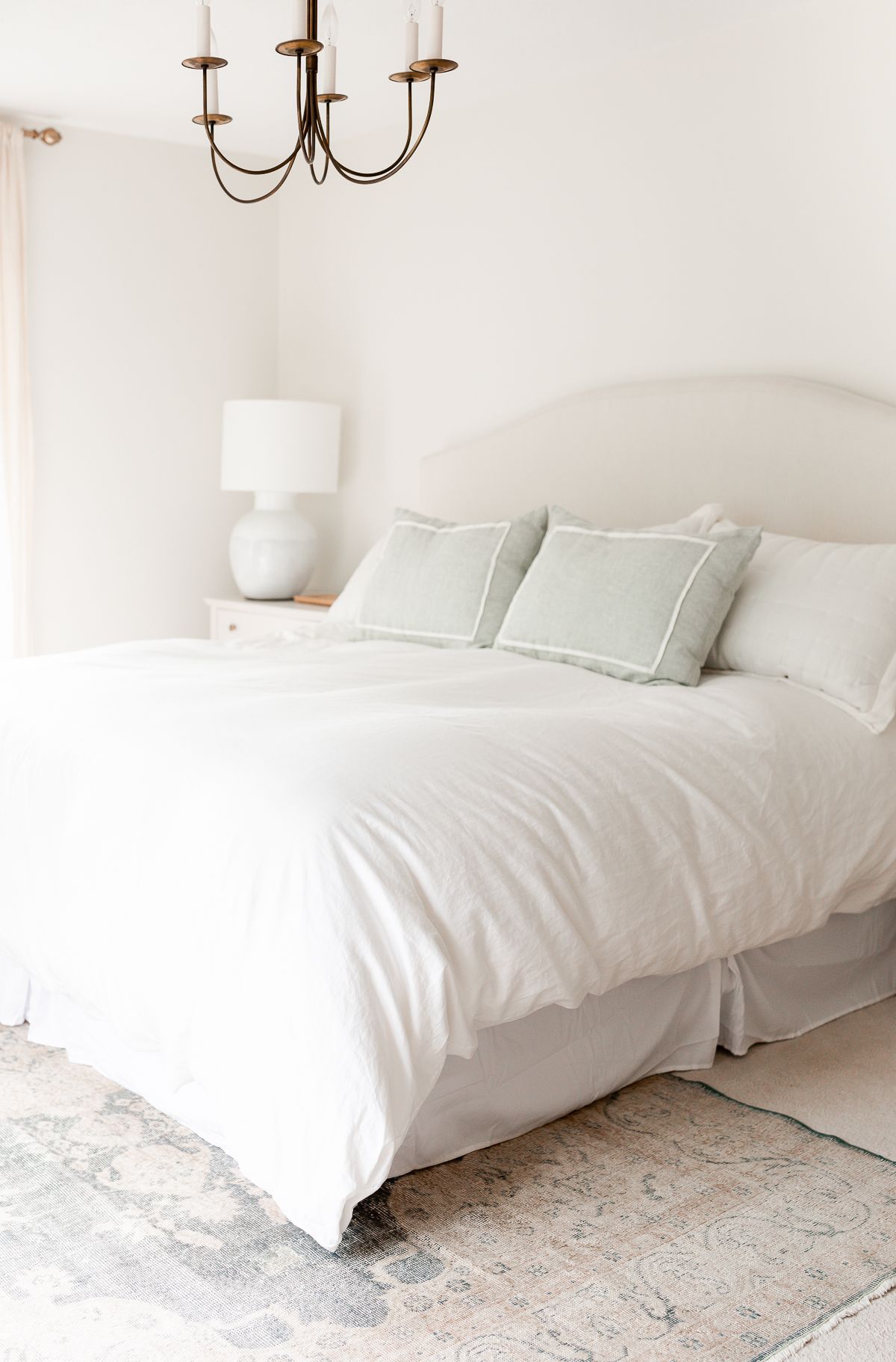 A white bedroom with a soft blue Turkish rug on the floor, over carpet.