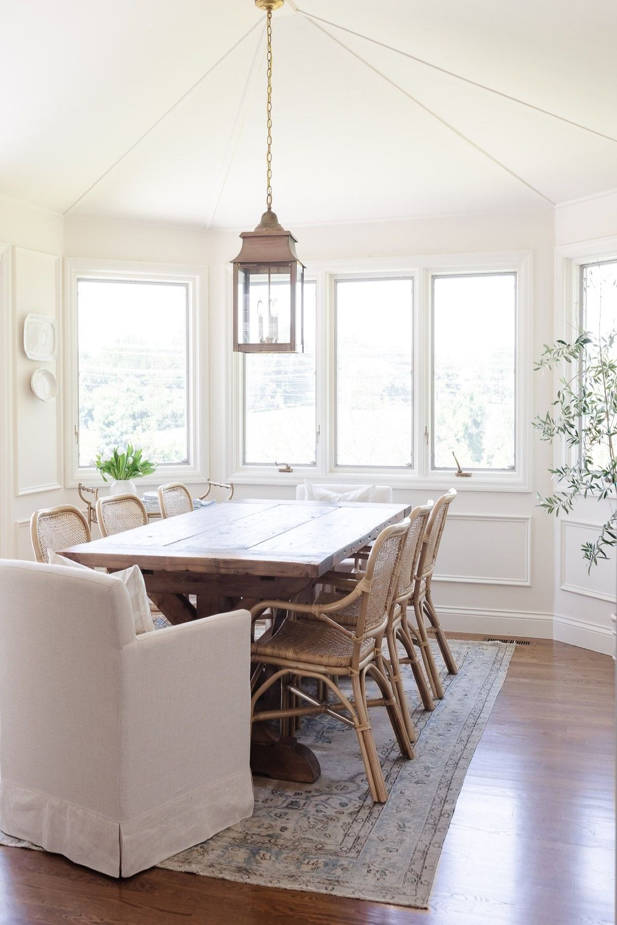 A white dining room with a rustic wood table and a vintage rug on the floor.