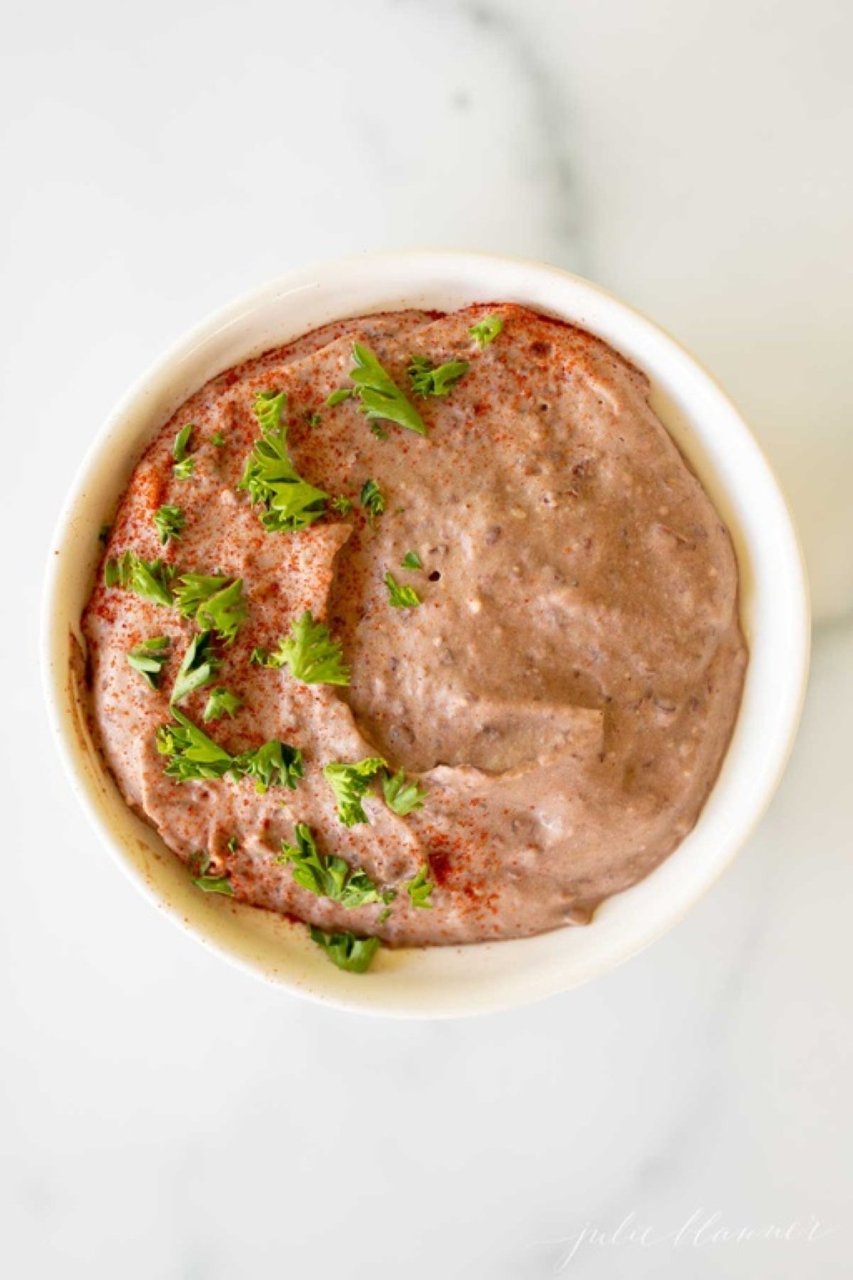 A white bowl of black bean hummus on a white marble countertop.