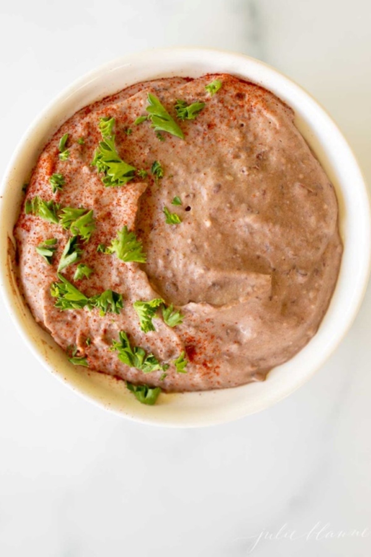 A white bowl of black bean hummus on a white marble countertop.