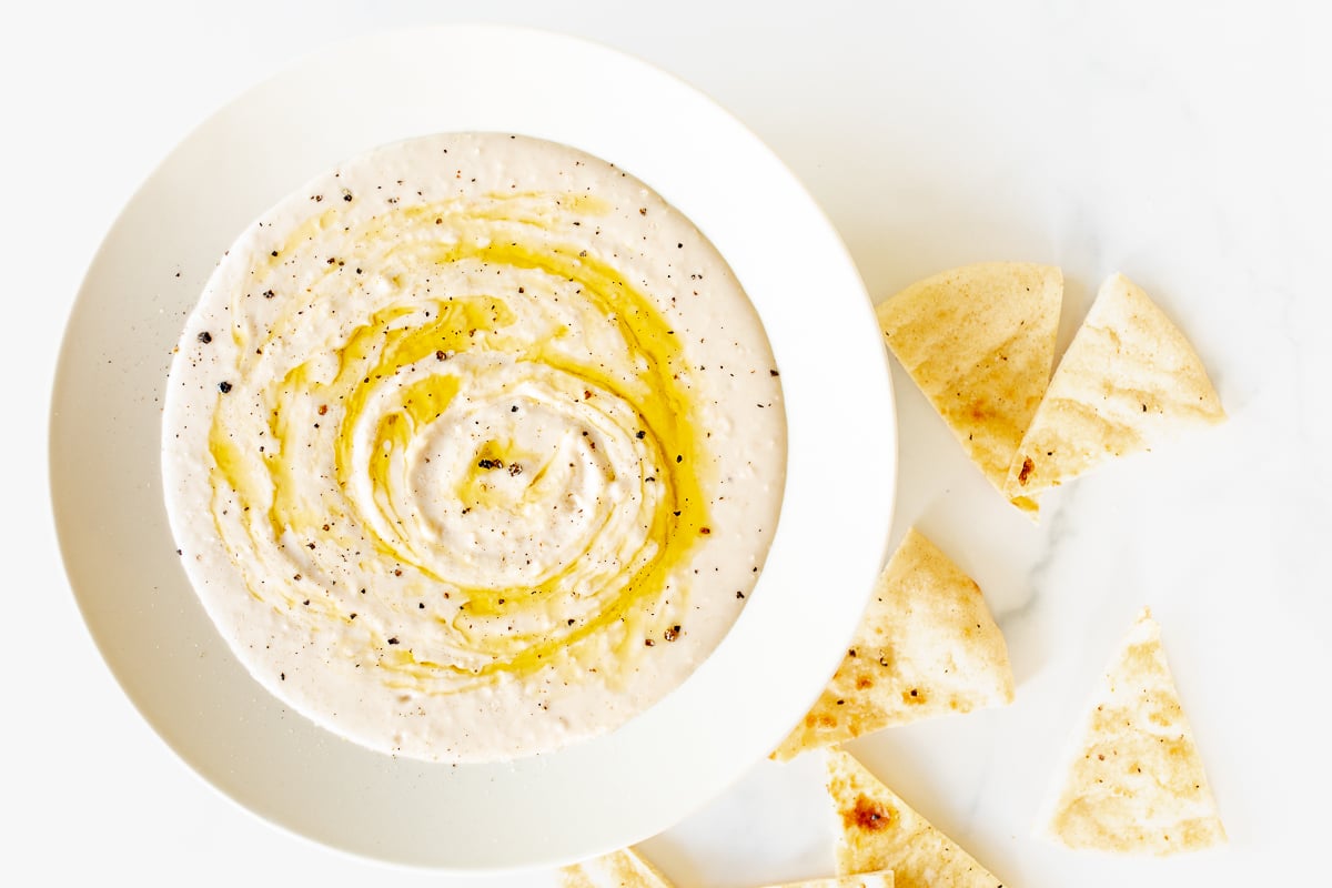 A white bowl of white bean hummus and pita bread to the side. 