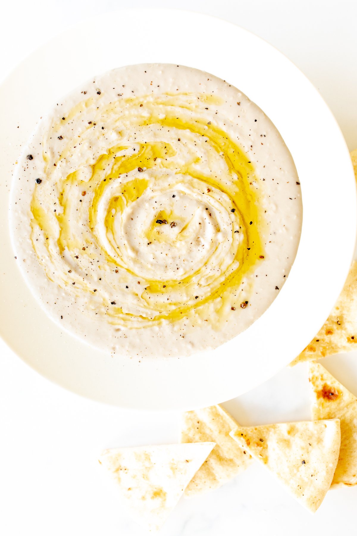 A white bowl of white bean hummus and pita bread to the side.