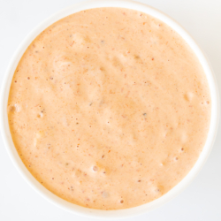 A white bowl of chipotle aioli on a white marble countertop.