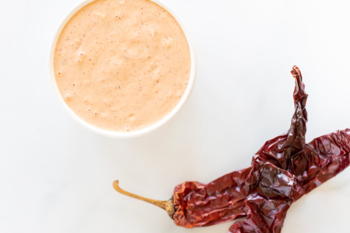 A white bowl of chipotle mayo with chipotle pepper in background.