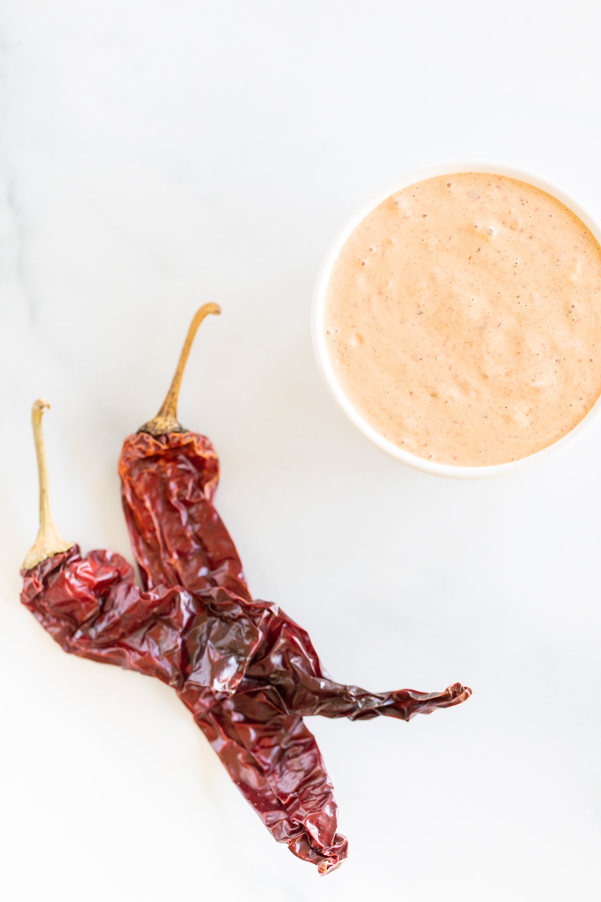 A white bowl of chipotle mayo with chipotle pepper in background.