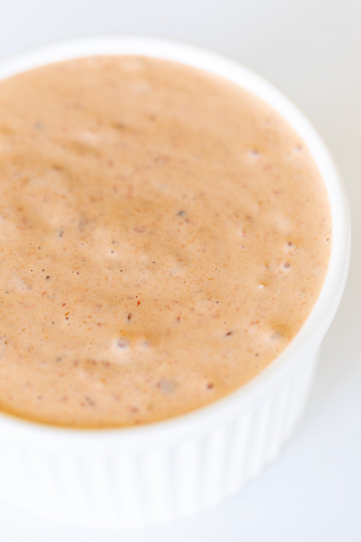 A white bowl of chipotle aioli on a white marble countertop.