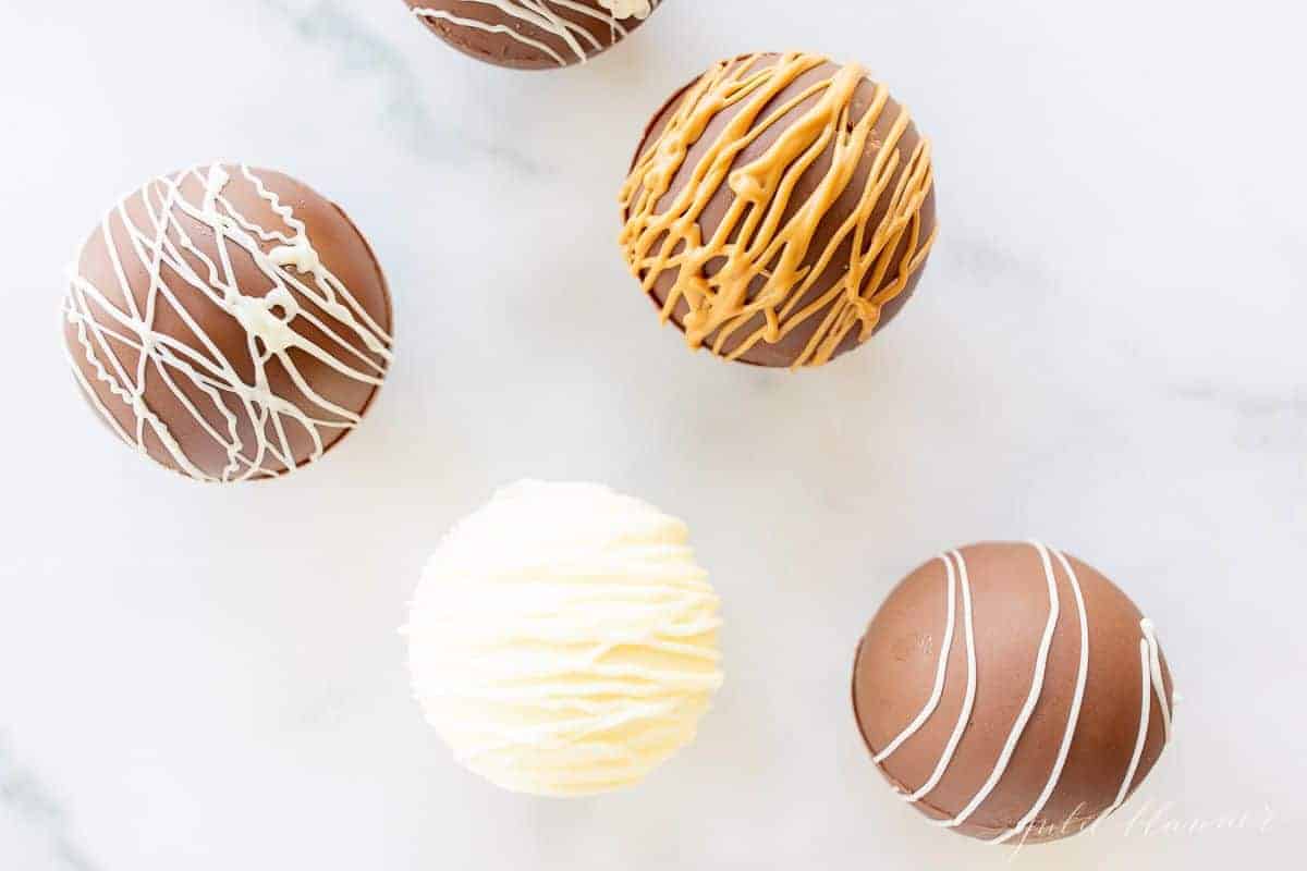 Peanut butter hot chocolate bombs on a marble surface, drizzled with peanut butter and white chocolate.