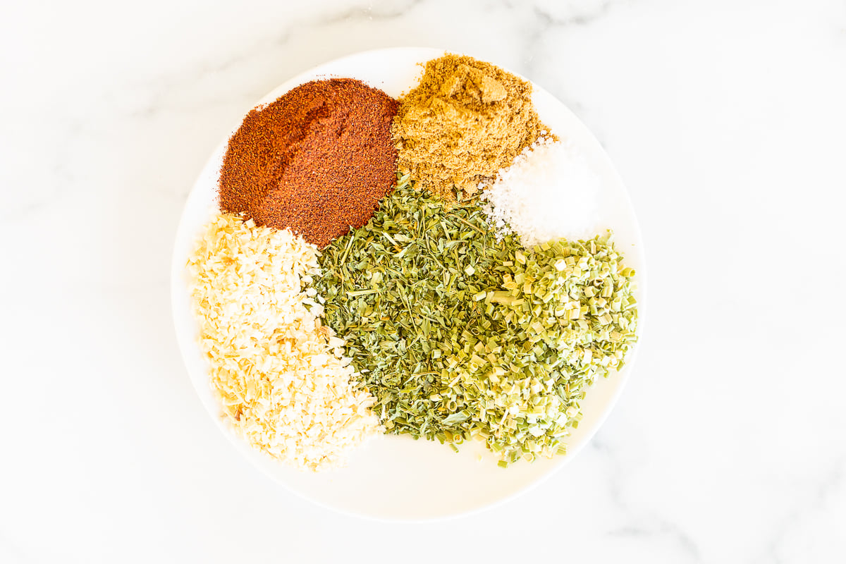 A white plate on a marble surface, topped with individual piles of spices for a homemade fiesta ranch mix.