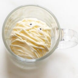 A white mummy Halloween hot chocolate bomb in a clear glass mug on a marble surface.