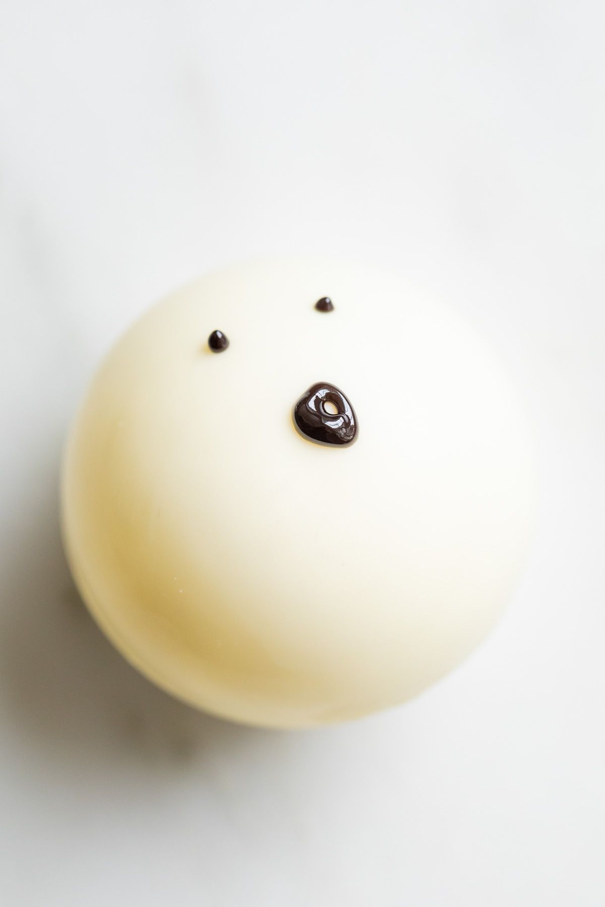 A white chocolate hot cocoa bomb, decorated as a ghost face.