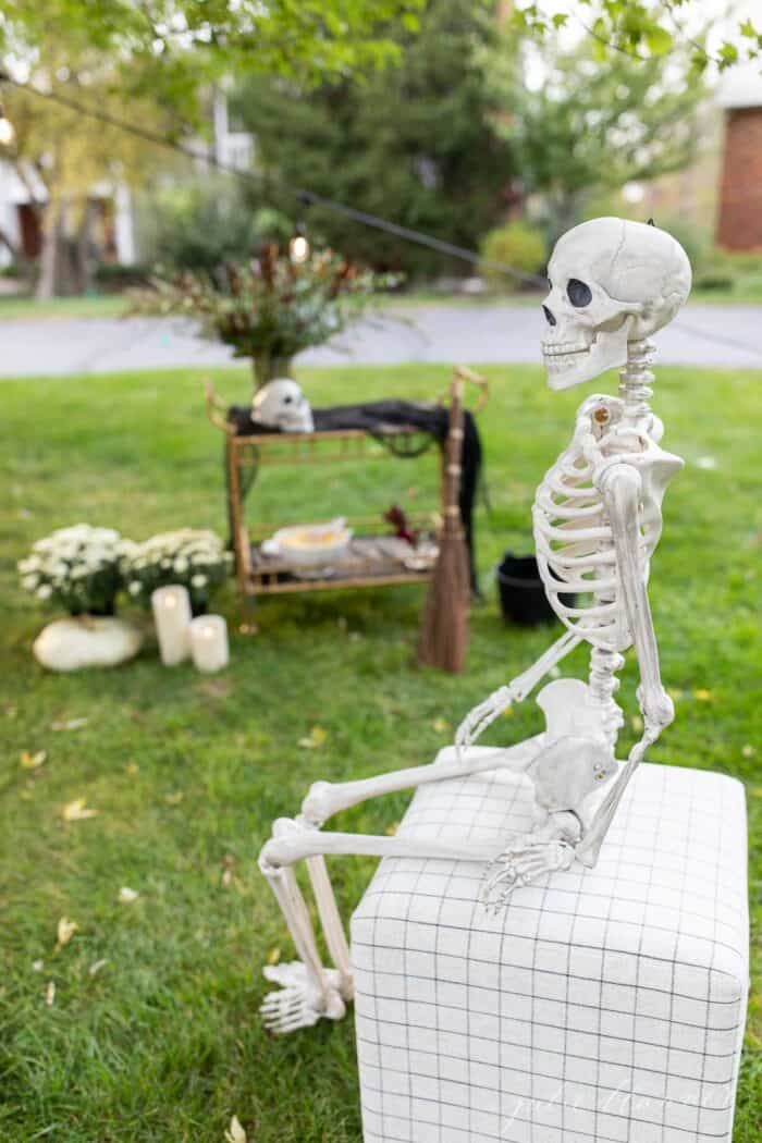 A skeleton sitting on a stool with a Halloween party set up in the background.