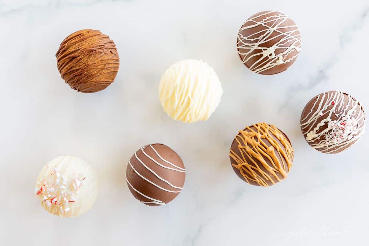 A marble surface with hot chocolate bombs in different colors and decorated styles.