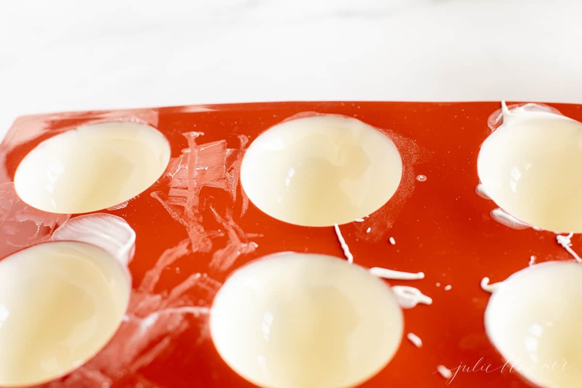 A red silicone sphere mold filled with white chocolate to make peppermint hot chocolate bombs.