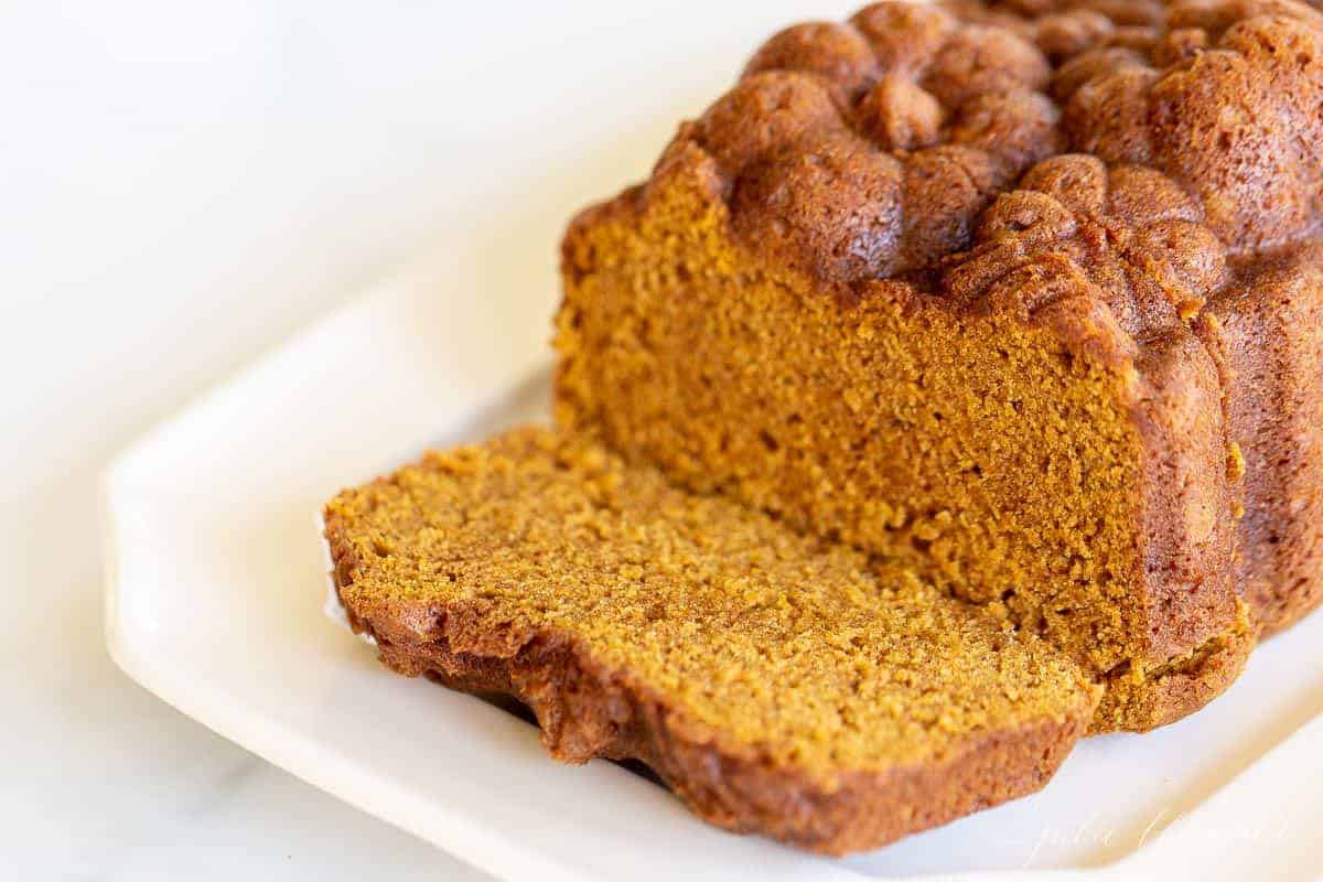 A white platter featuring a loaf of pumpkin bread with a slice cut at the front.