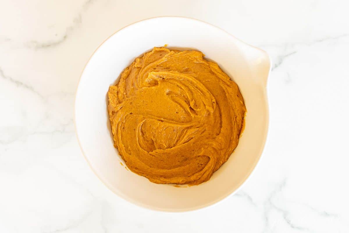 A white bowl full of pumpkin cheesecake bread batter.