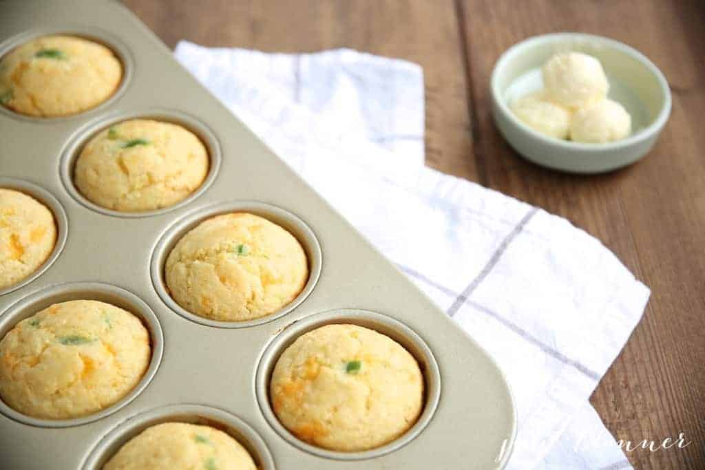 A gold muffin pan full of jalapeno cheddar cornbread muffins, pats of butter to the side 