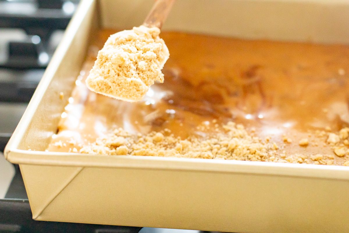 A spoon dropping an oatmeal topping onto a pan of cookie bars