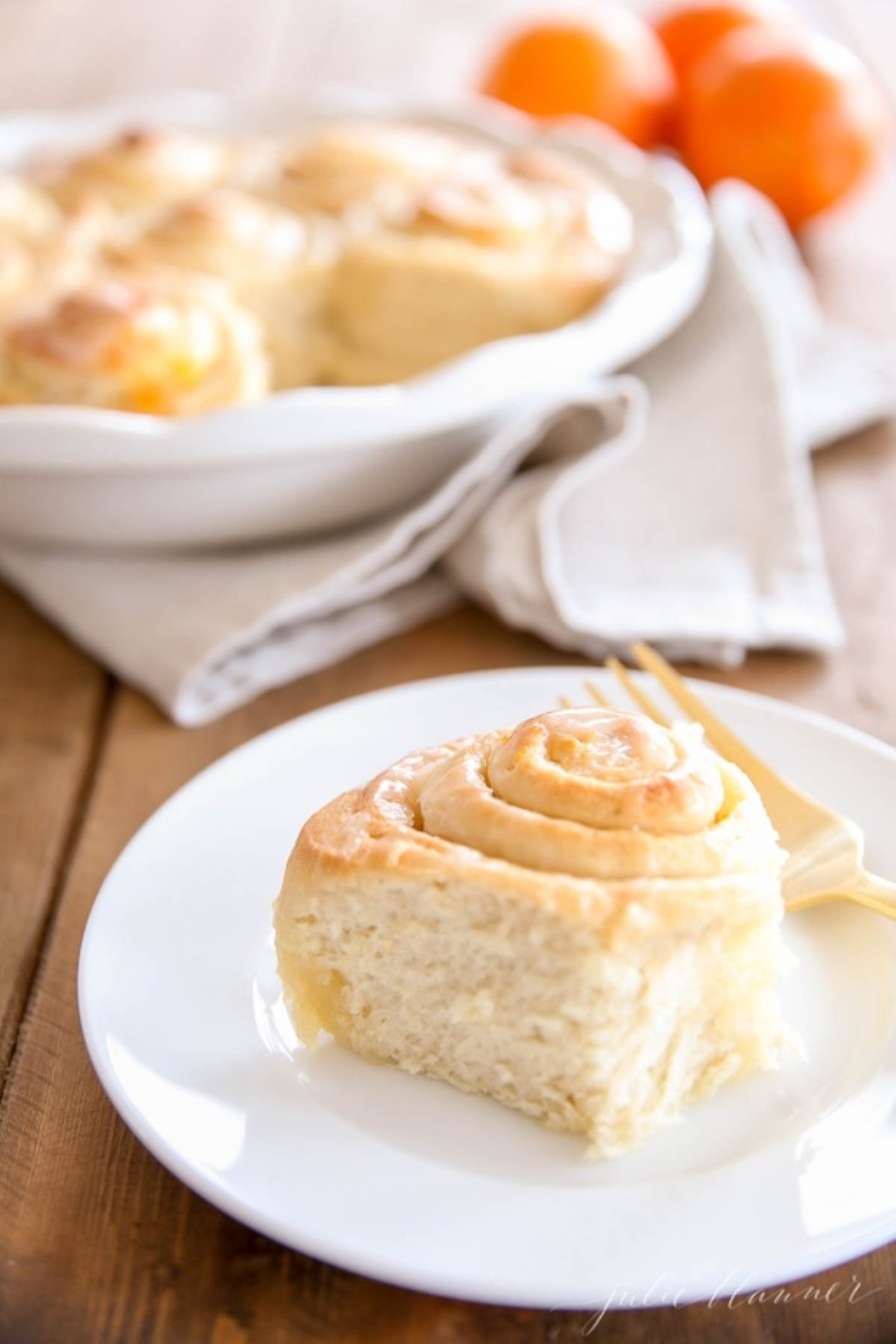 An orange roll covered in orange glaze on a white plate.