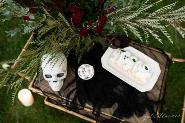 Halloween outdoor movie night snacks set up on a gold bar cart, flowers in the background.