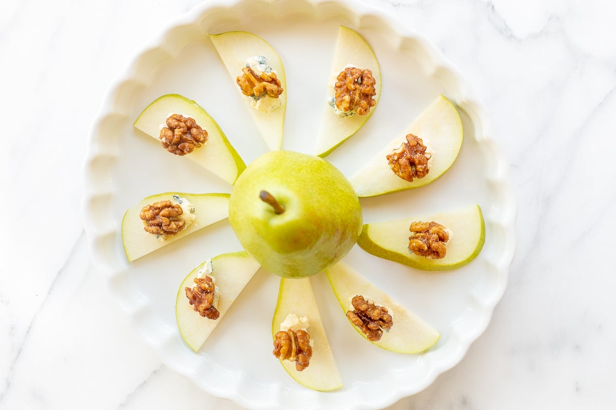 Walnut, blue cheese and sliced pear appetizers on a white platter.