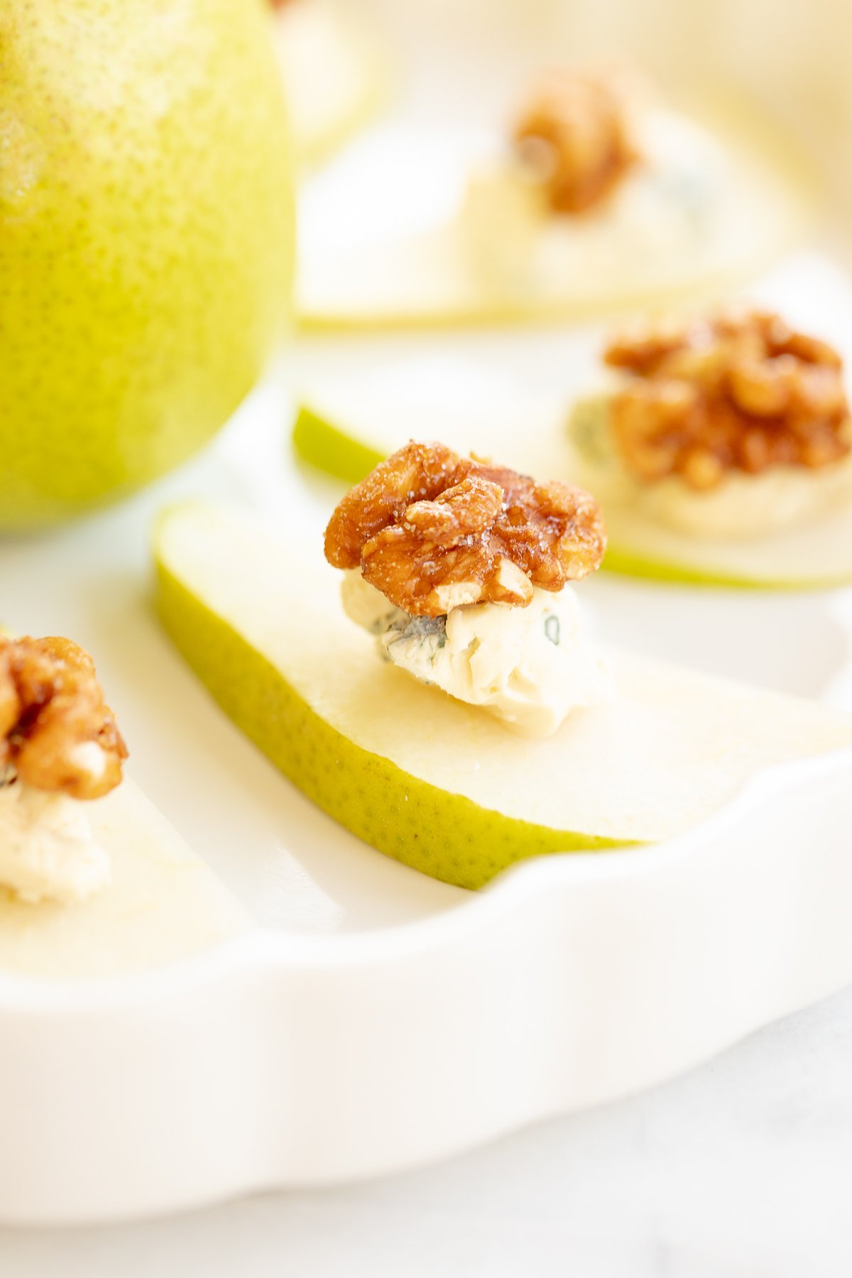 Walnut, blue cheese and sliced pear appetizers on a white platter.