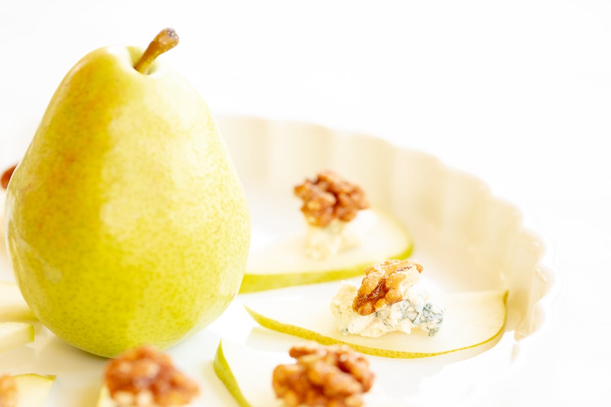 Walnut, blue cheese and sliced pear appetizers on a white platter.