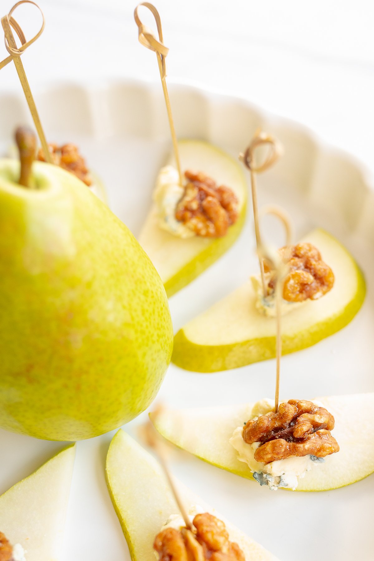 Walnut, blue cheese and sliced pear appetizers on a white platter.