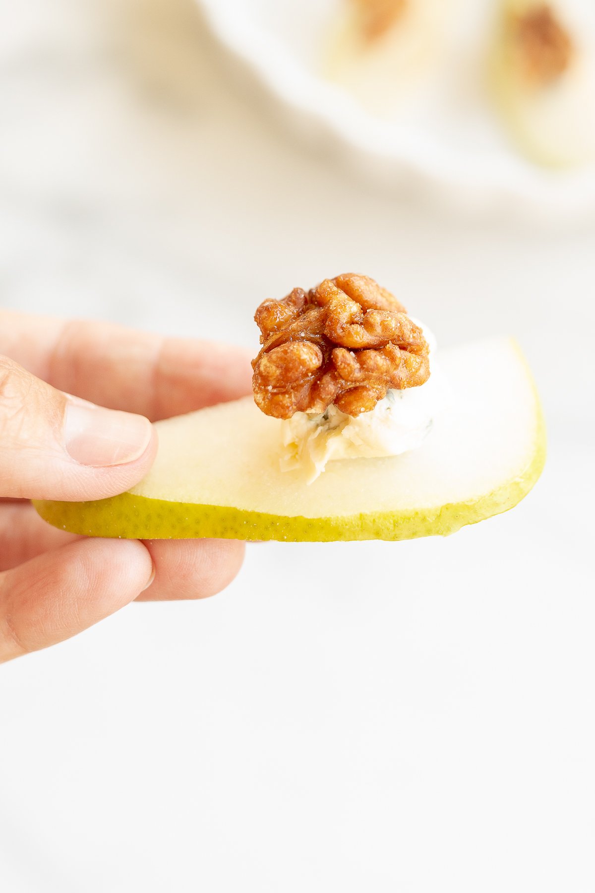 A hand holding a slice of pear topped with a walnut and blue cheese.