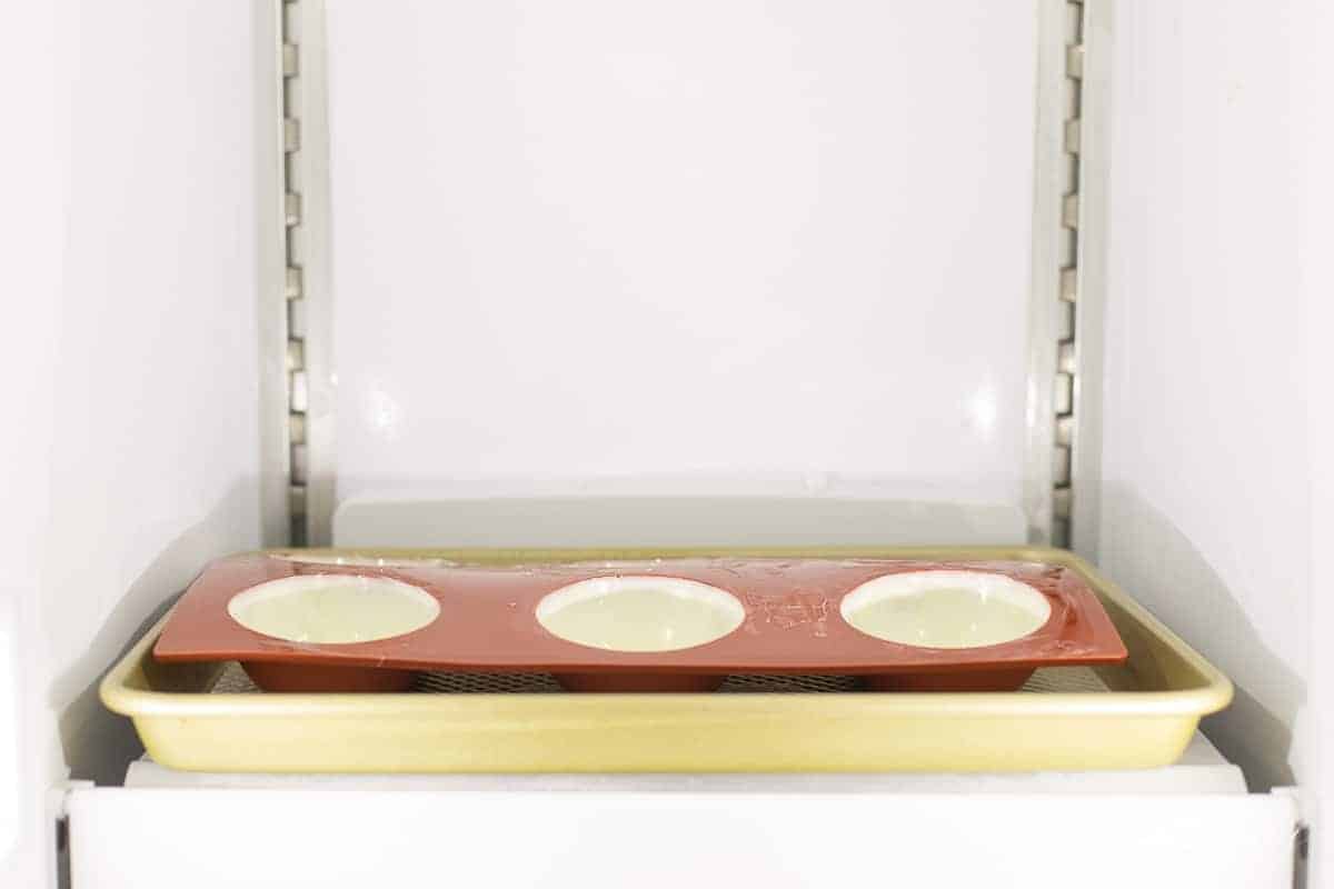 Looking inside a freezer with a silicone mold filled with white chocolate spheres.