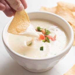 tortilla chip dipped in queso blanco dip in a white bowl