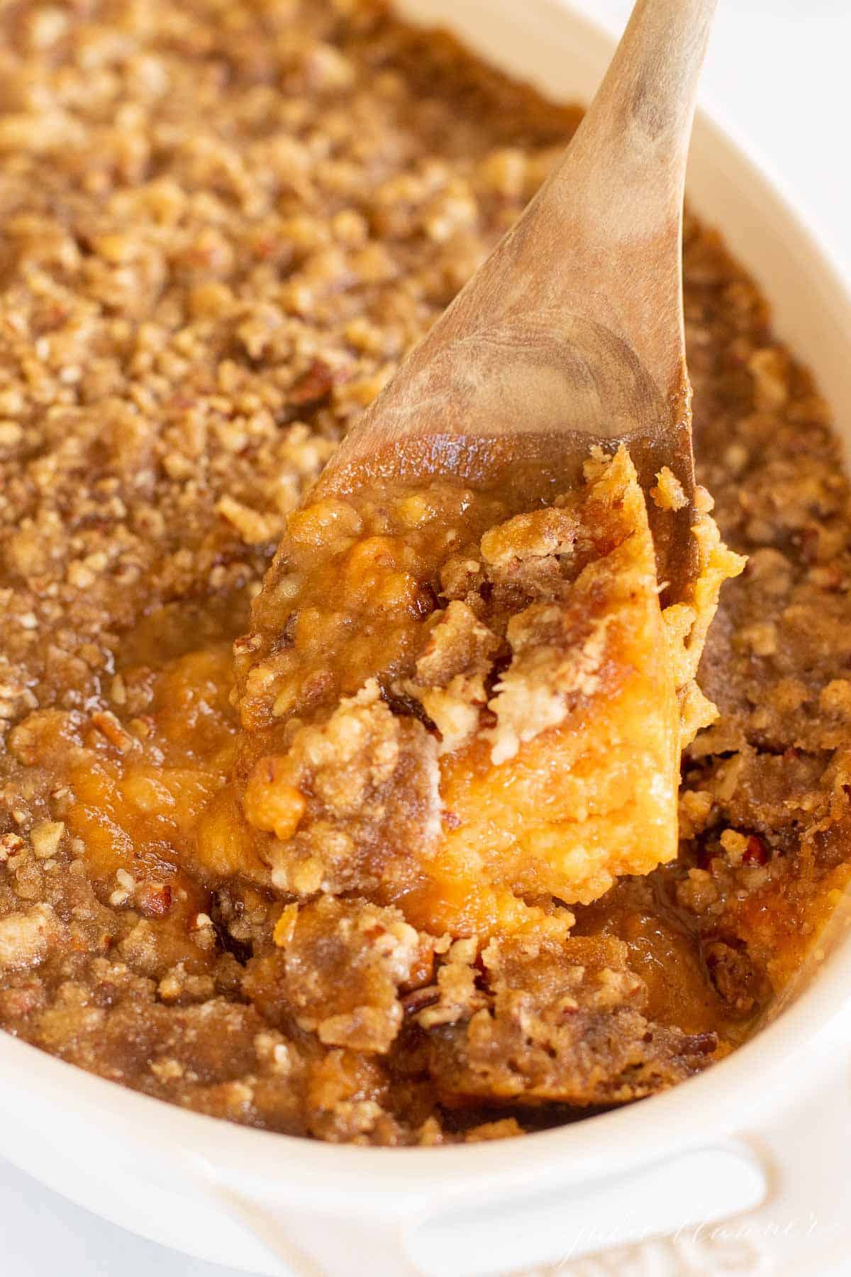 A white oval baking dish filled with a sweet potato casserole, spoon lifting out a serving.