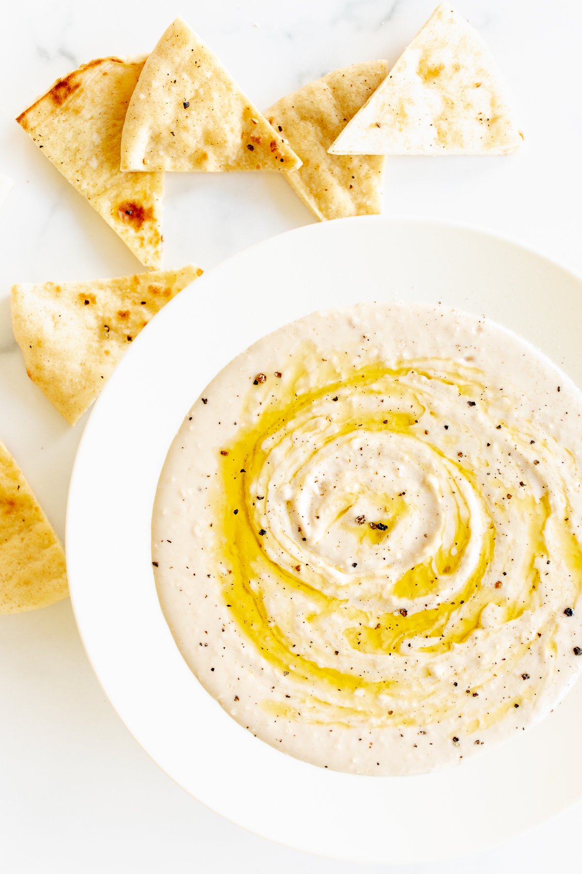 A white bowl of white bean dip and pita bread to the side.