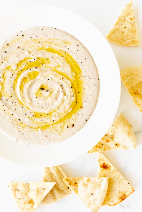 A white bowl of white bean dip and pita bread to the side.