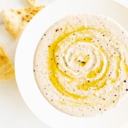 A white bowl of white bean dip and pita bread to the side.