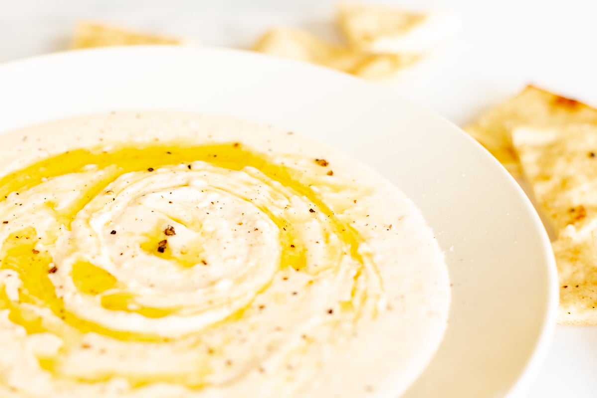 A white bowl of white bean dip and pita bread to the side.