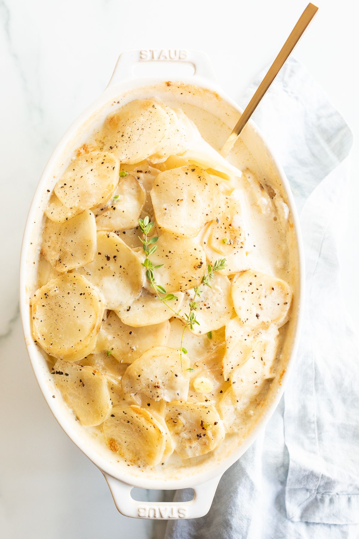 Gratin Dauphinoise potatoes in a white oval baking dish, garnished with fresh thyme.
