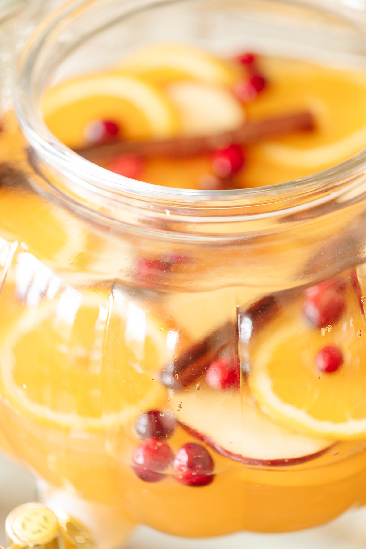 A clear glass pumpkin drink dispenser filled with apple cider sangria.