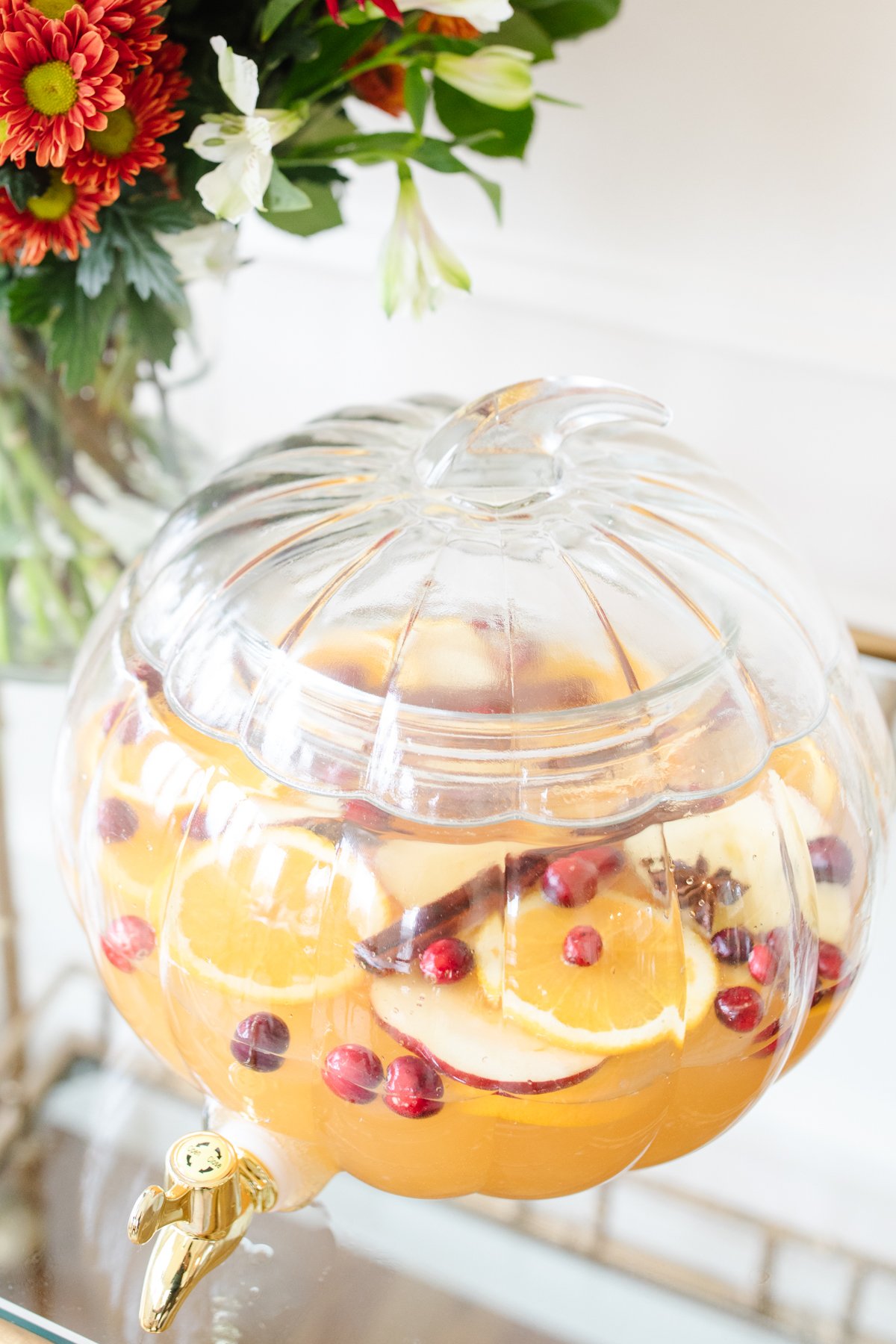 A clear glass pumpkin drink dispenser filled with apple cider sangria.