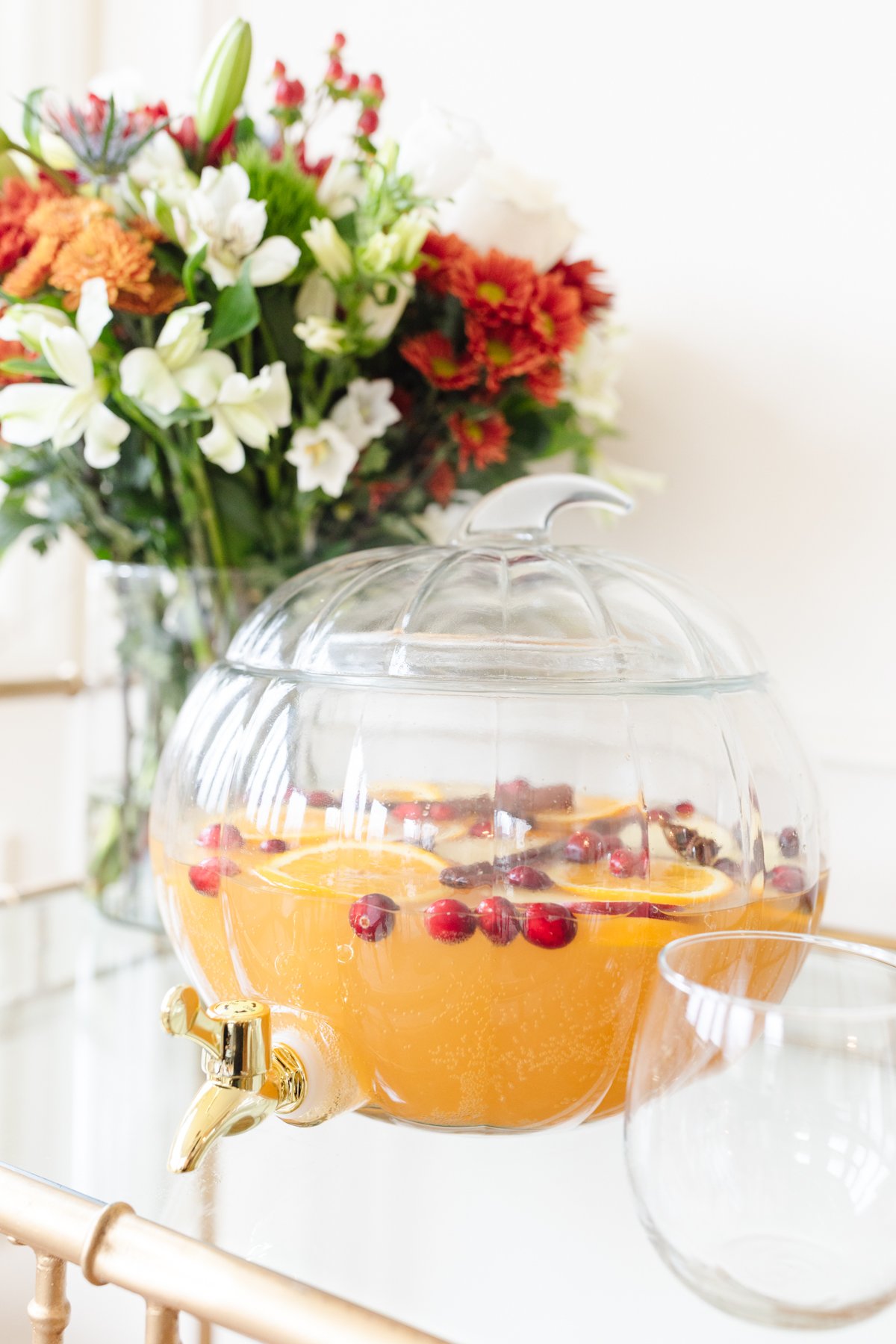 A clear glass pumpkin drink dispenser filled with apple cider sangria.