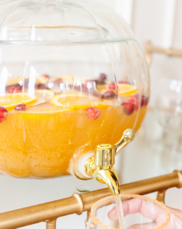 A clear glass pumpkin drink dispenser filled with apple cider sangria.